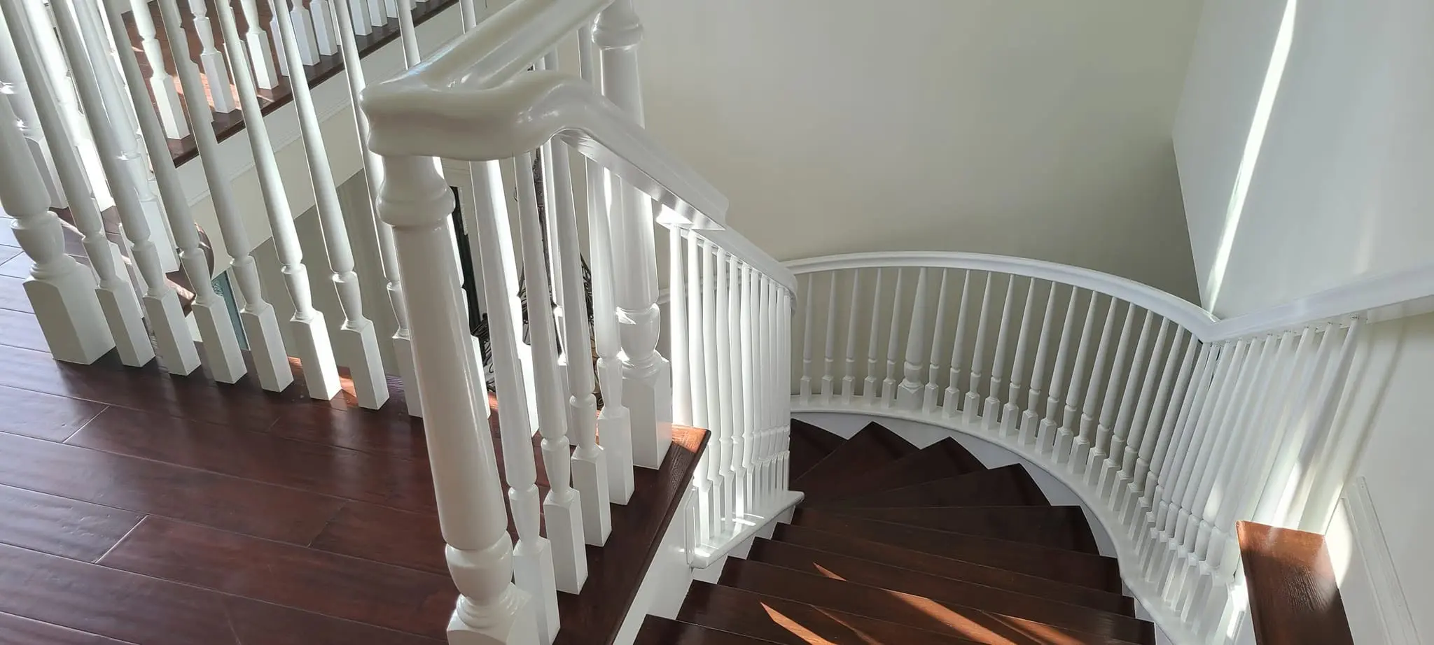 White curved stair railing and newel post over refinished hardwood flooring
