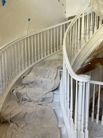Curved staircase fully masked with drop cloths before spraying the railing