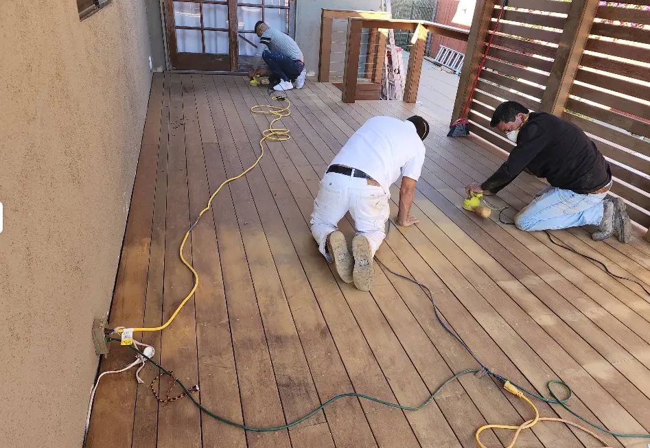 Two painters staining a hardwood deck floor on a covered patio