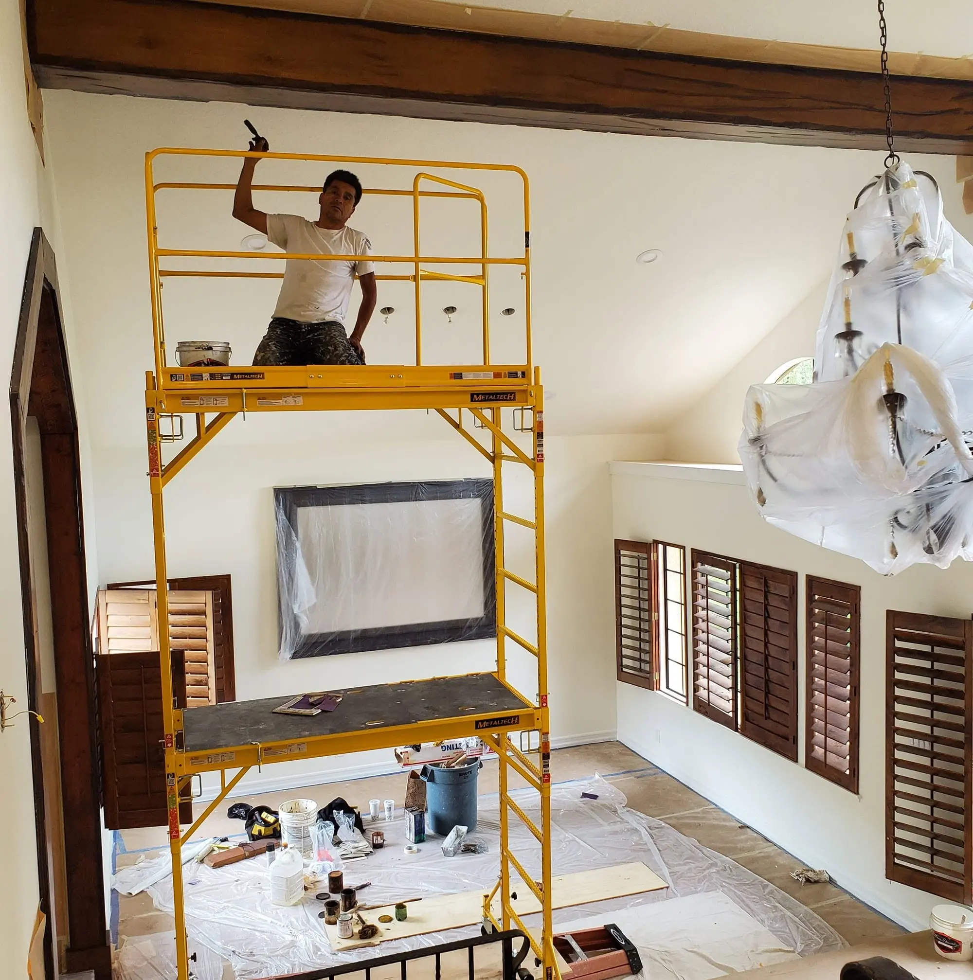 Painter on a rolling scaffold coating a two-story living room wall in a Panorama City home