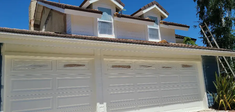 Three white garage doors and tile-roof facade after an exterior repaint