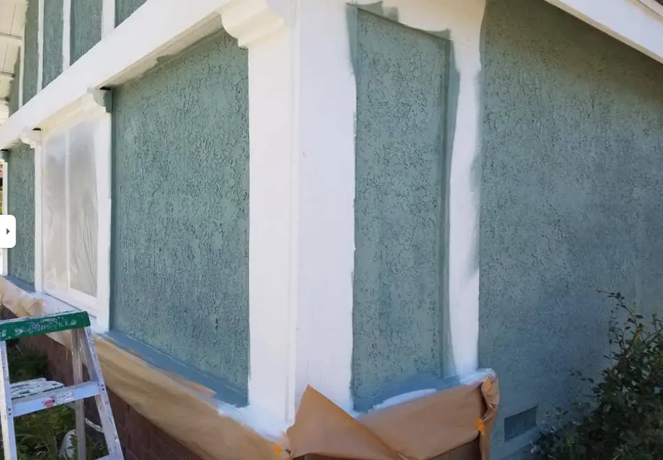 Teal stucco exterior wall with windows masked off during an exterior painting job