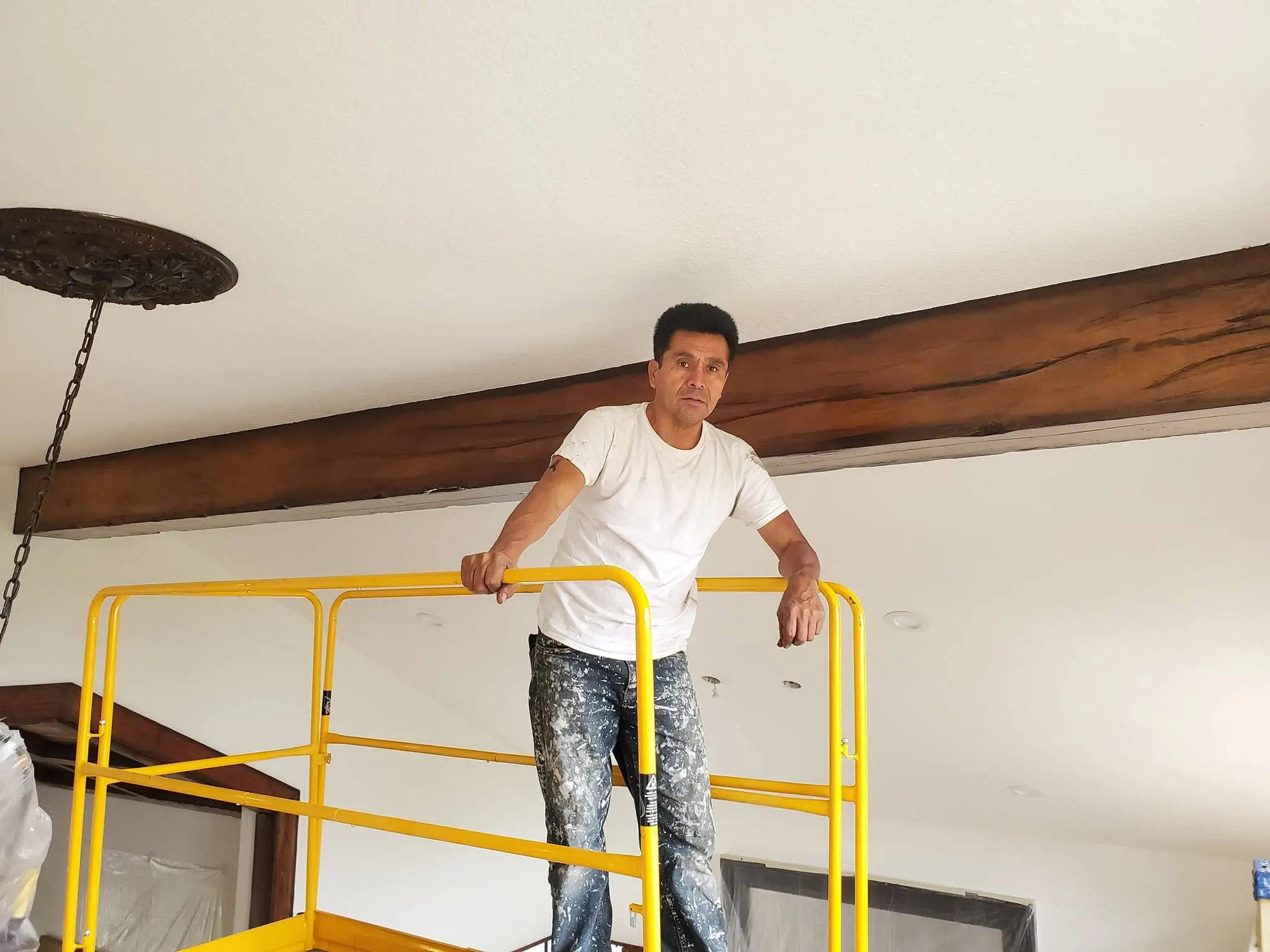 Painter standing on scaffolding beneath a stained wood beam ceiling
