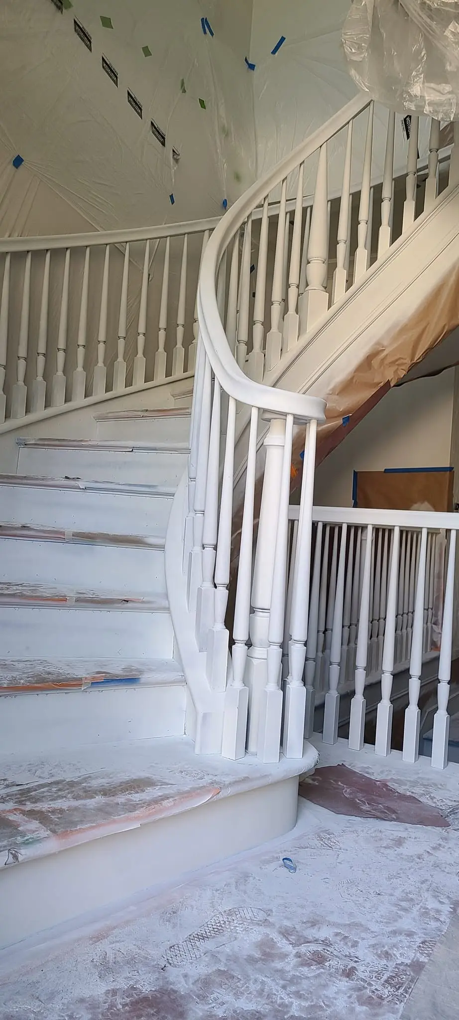 Curved staircase mid-project with primed spindles and protected treads