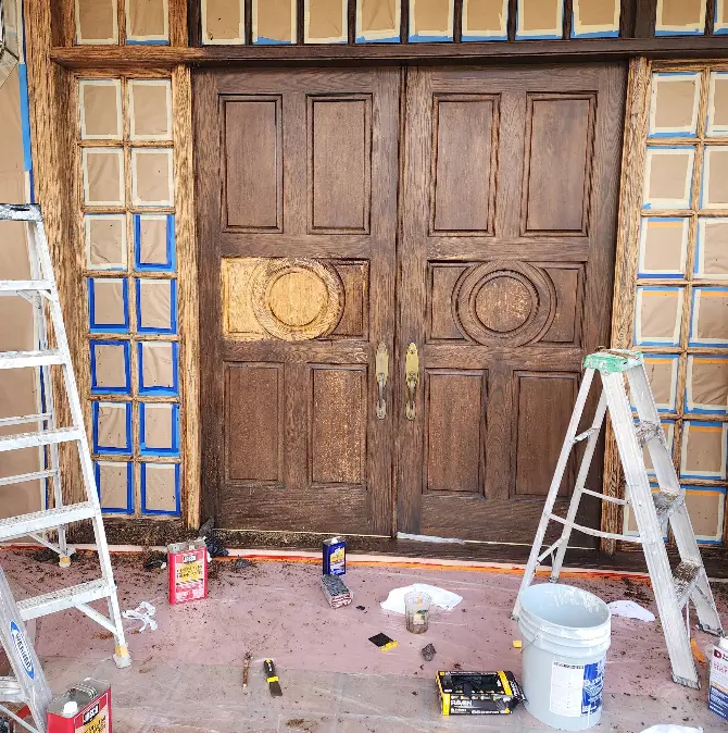 Carved double entry doors masked off and being refinished with wood stain