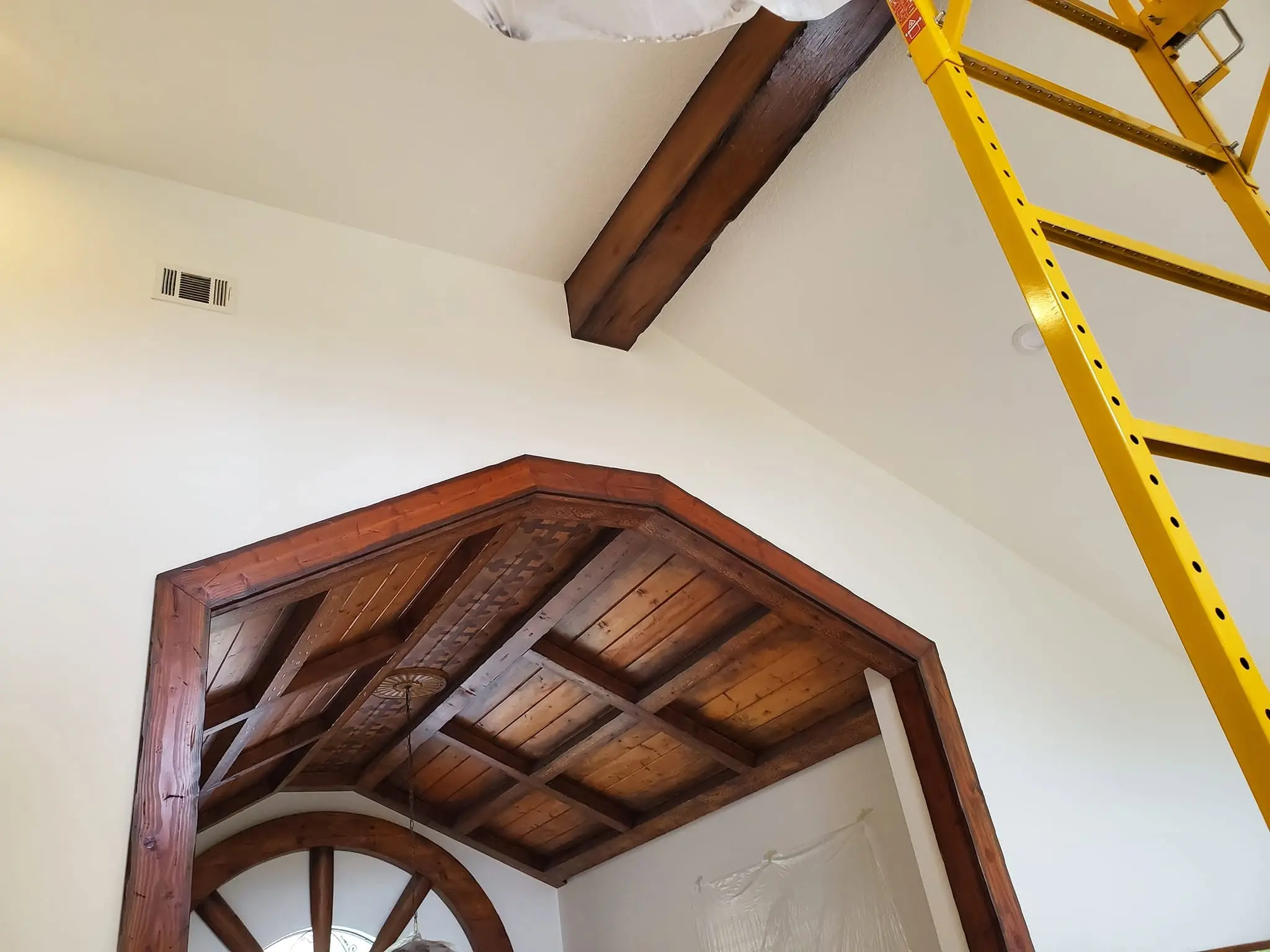 Dark-stained cathedral wood beam ceiling being refinished with an extension ladder in place